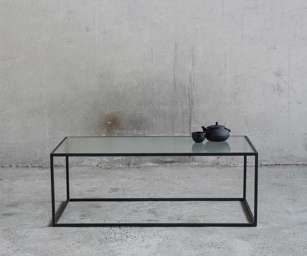 Ein Couschtisch aus Metall in Schwarz mit Tischplatte aus Drahtglas
